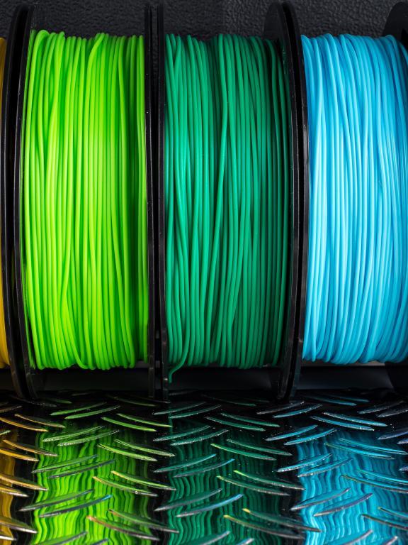 Side-by-side spools of rainbow-colored 3-D printer plastic