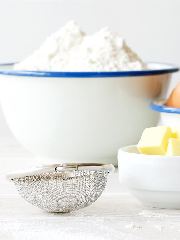Bowls of flour, butter cubes, brown eggs, powdered sugar, granulated sugar, and a sifter