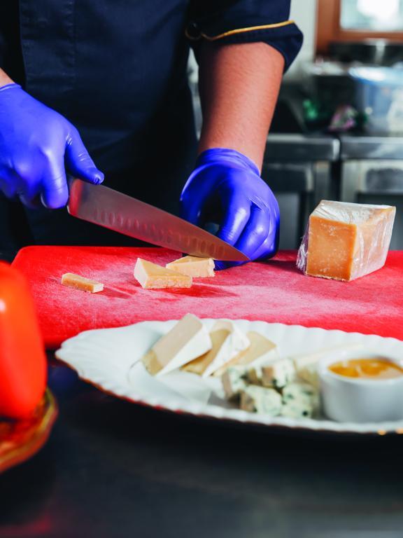 Chef in blue gloves slices cheese on red cutting board