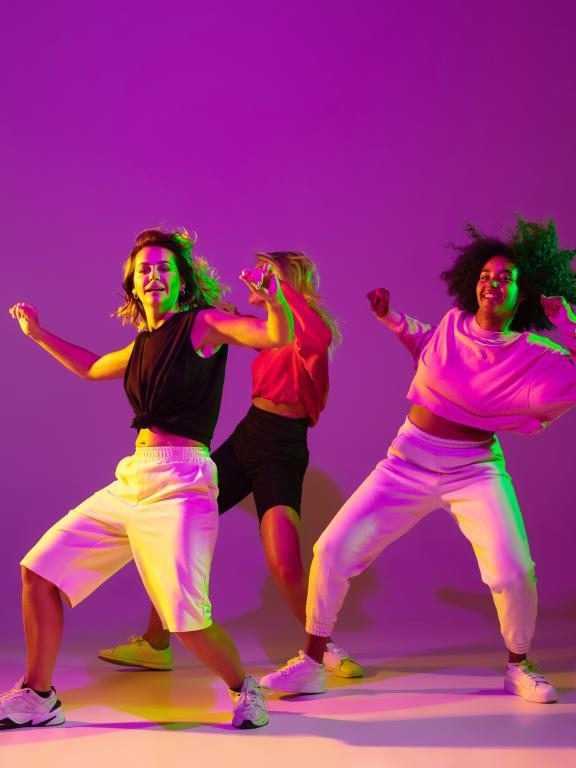 Three females dancing against purple background