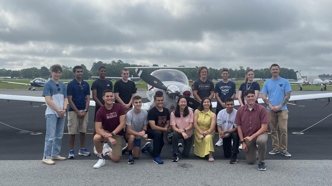 Fifteen students in flight school camp pose outside by small airplane