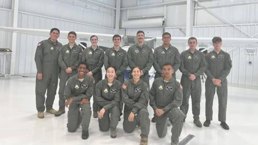 Twelve students in flight school camp pose in the hangar wearing flight suits