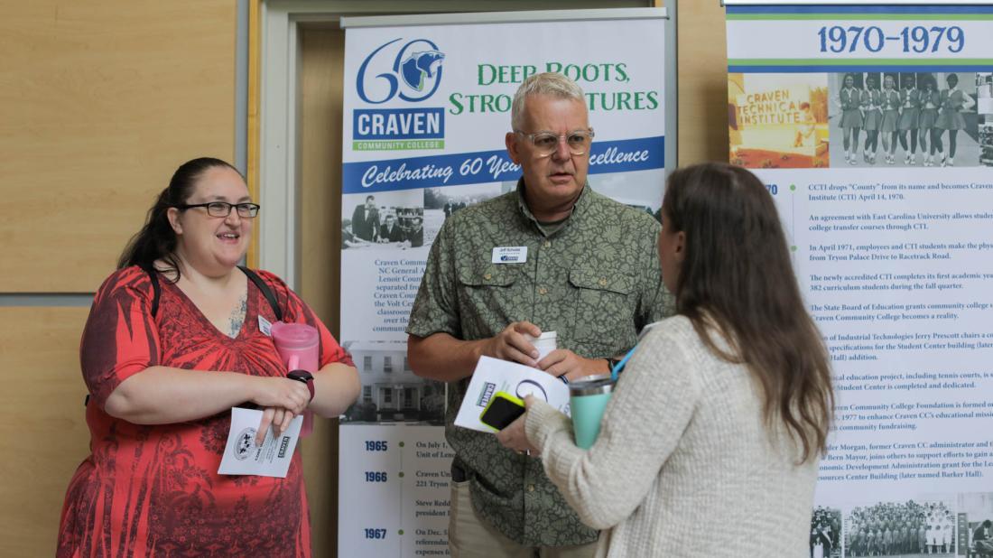 Three employees stand in front of banners of Craven's history