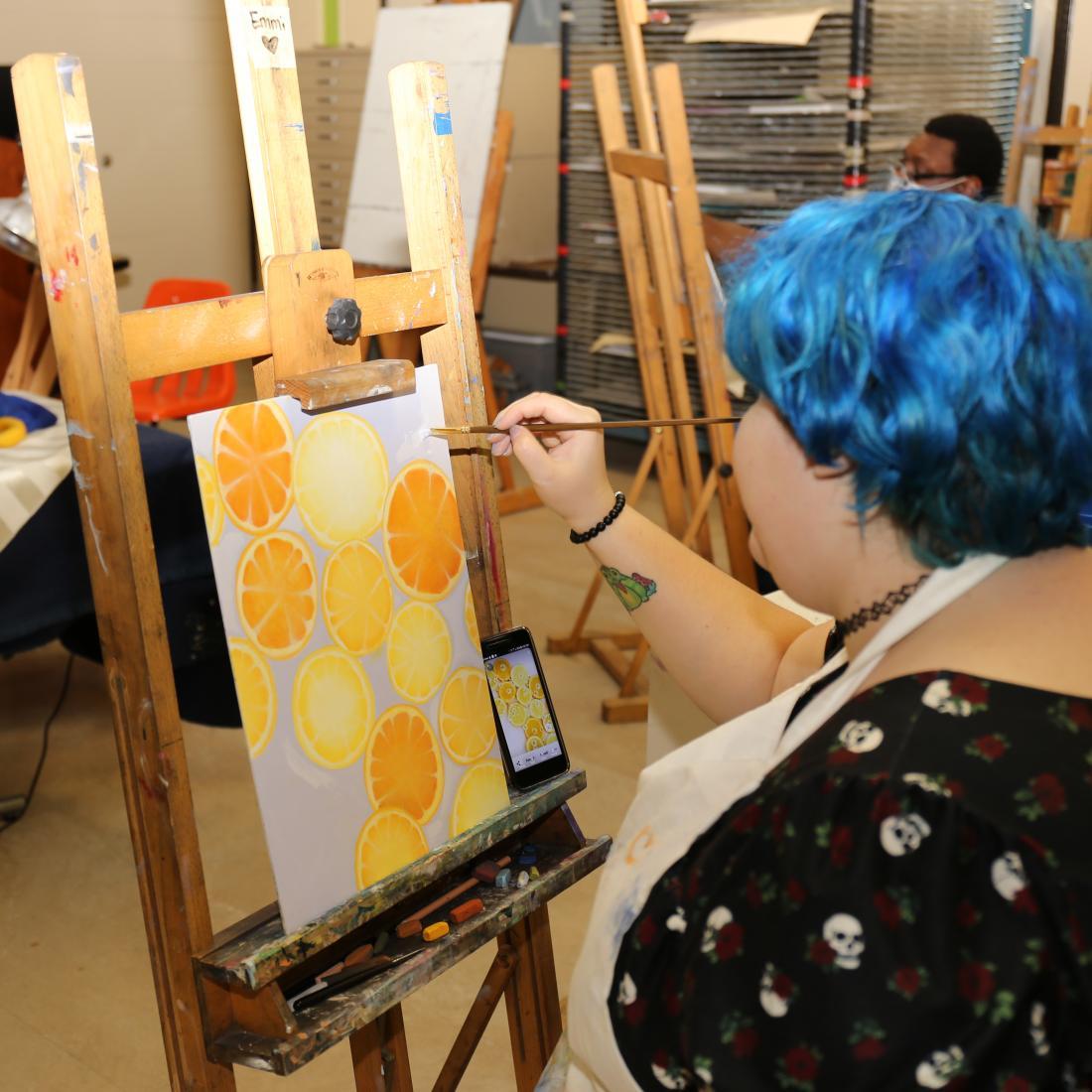blue haired female student at easel painting