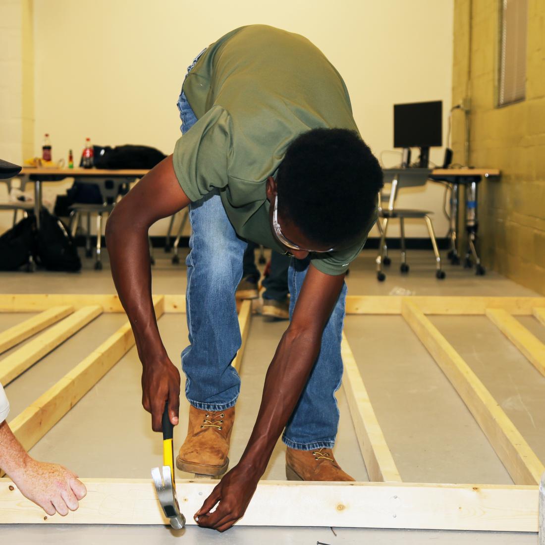 Two male carpentry students hammer boards