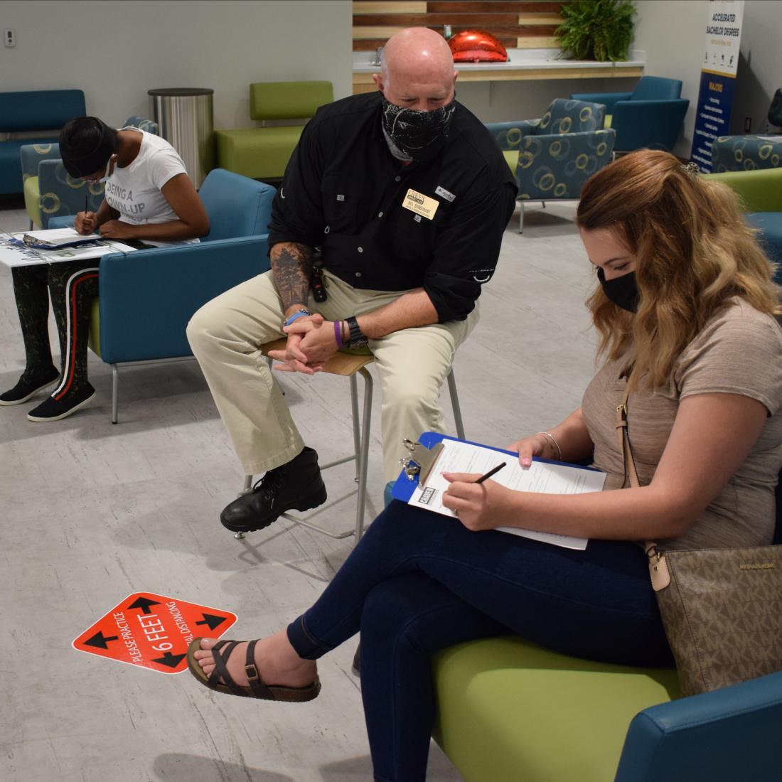 Advisor Bill Bondurant meets with a student while all wearing masks