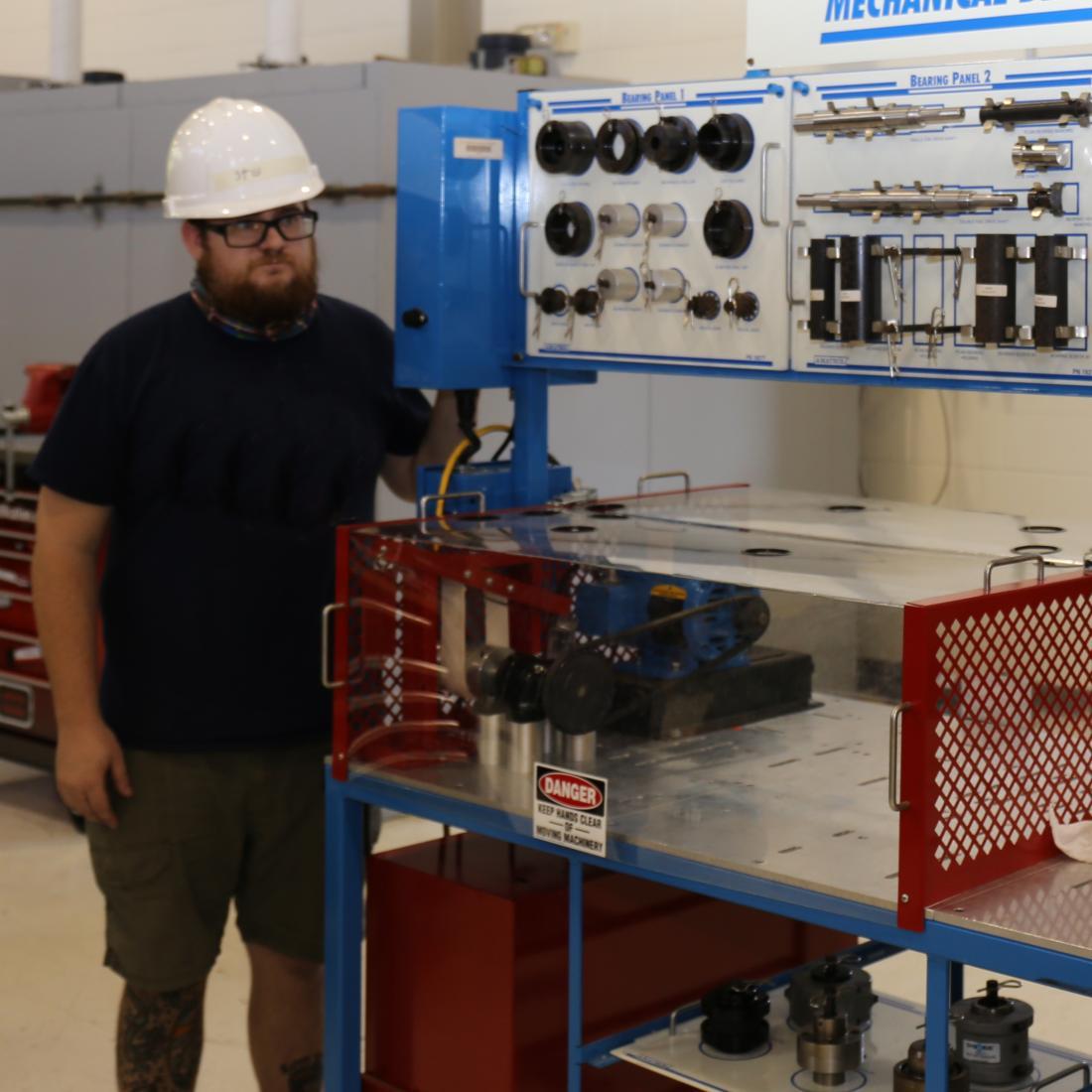 Student in hard hat stands by mechanical drive system