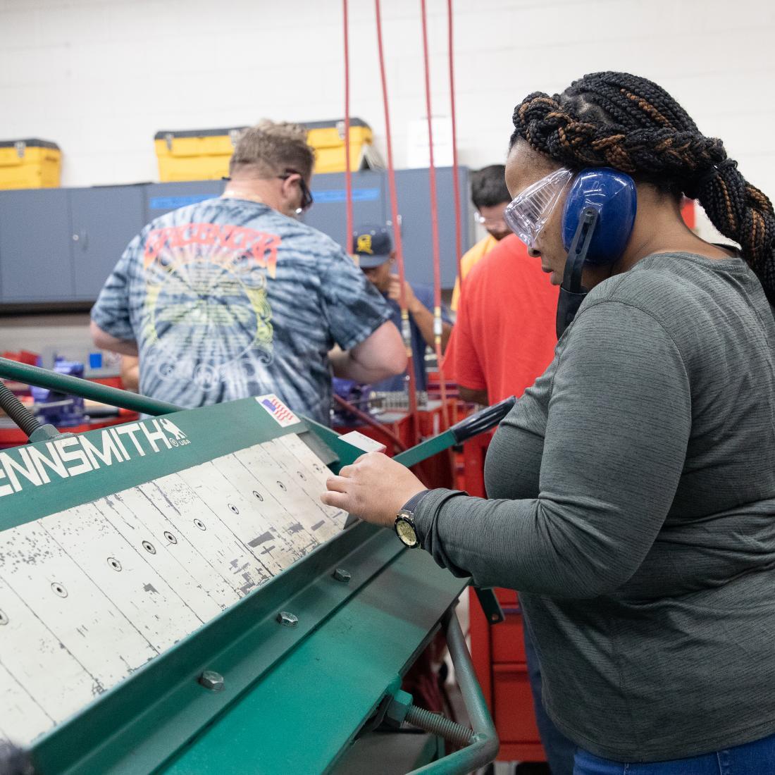 Woman in protective hearing muffs works on aircraft sheet metal