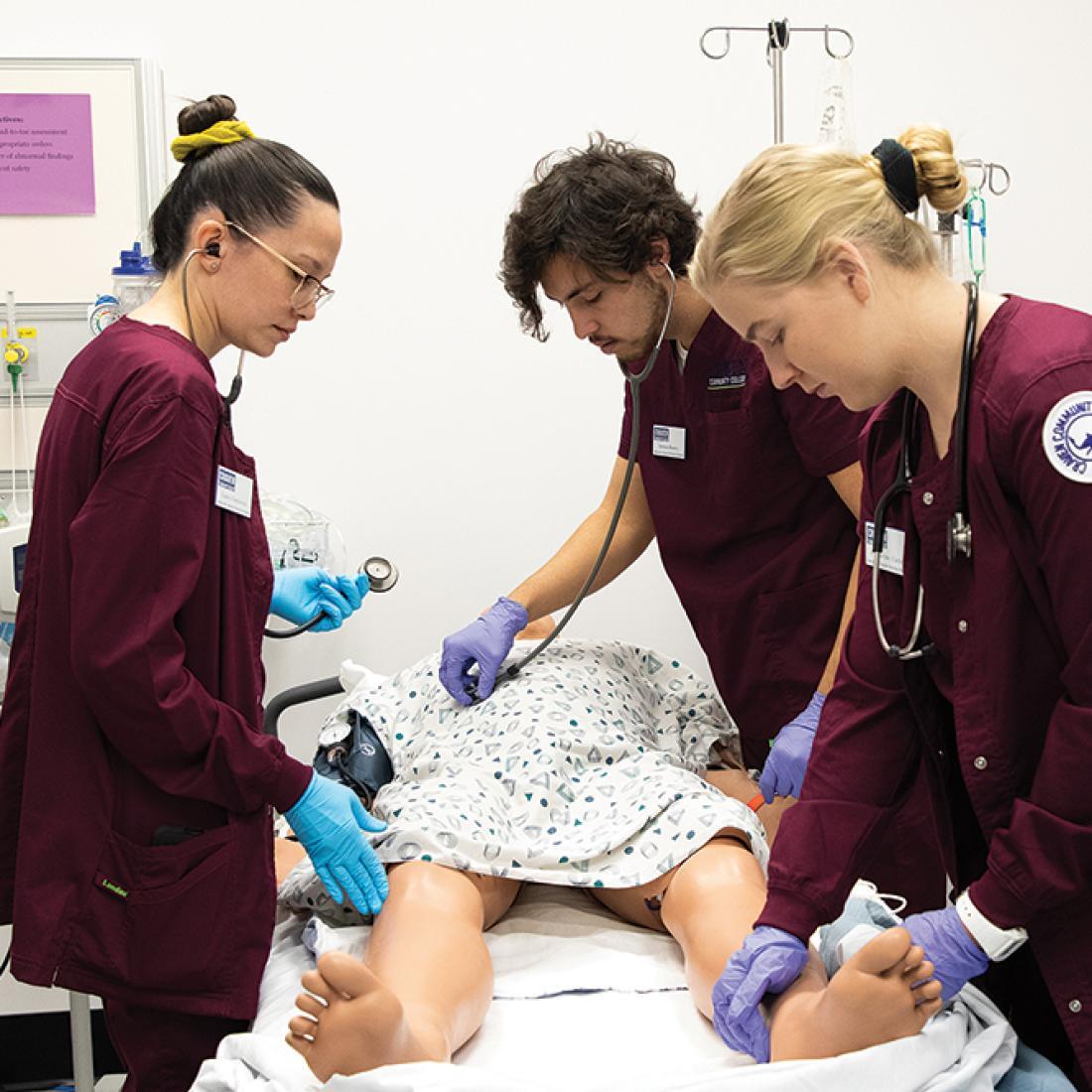 Three nursing students practice on a simulated patient