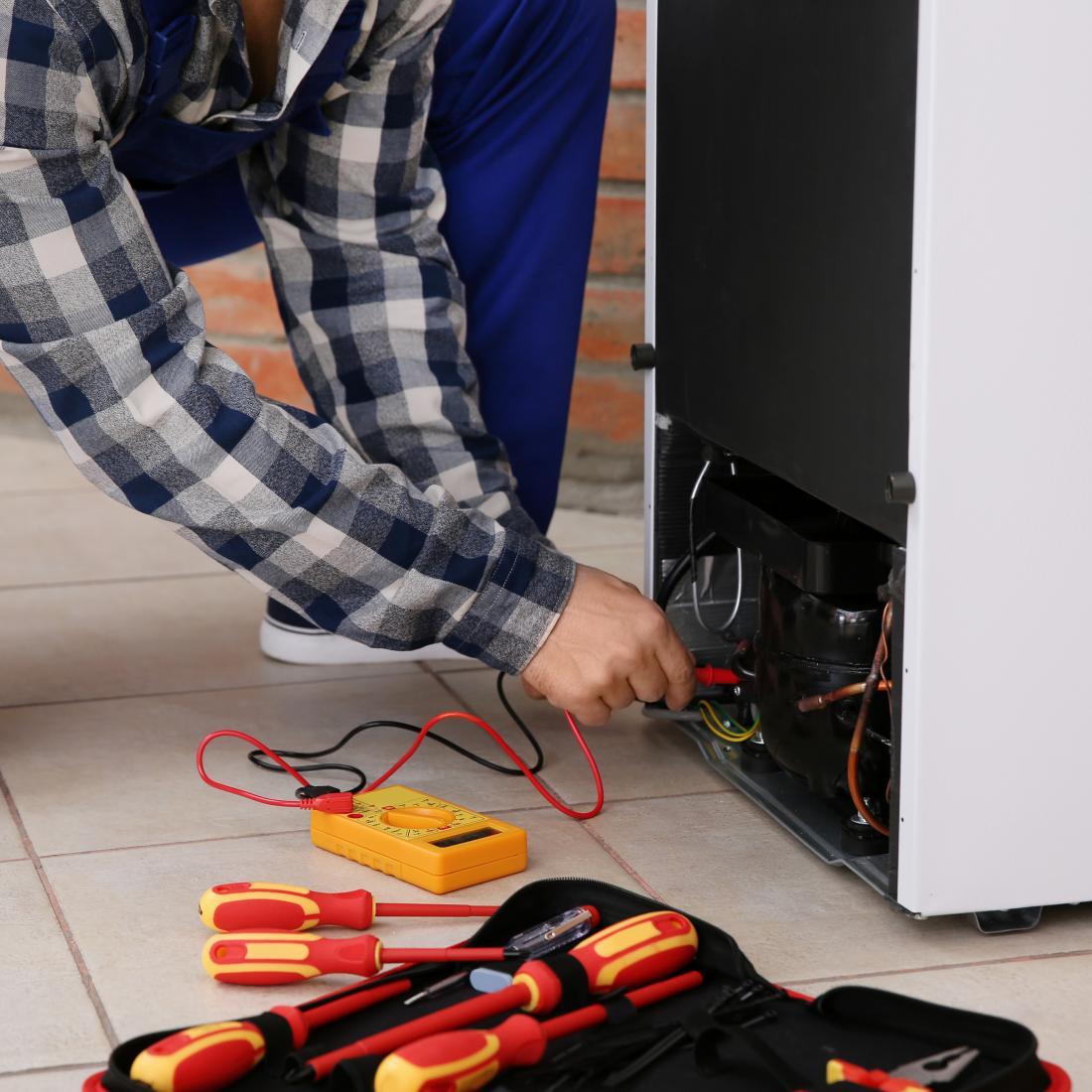 Male home appliance technician using multimeter and repairing broken refrigerator indoors