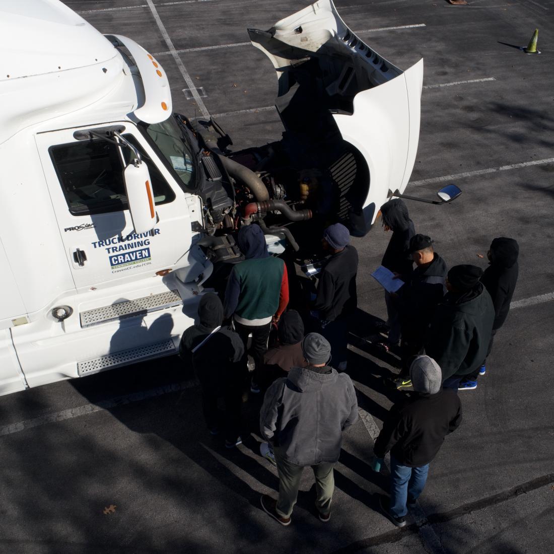 Group of students in the truck driver training program look under the hood on an 18 wheeler