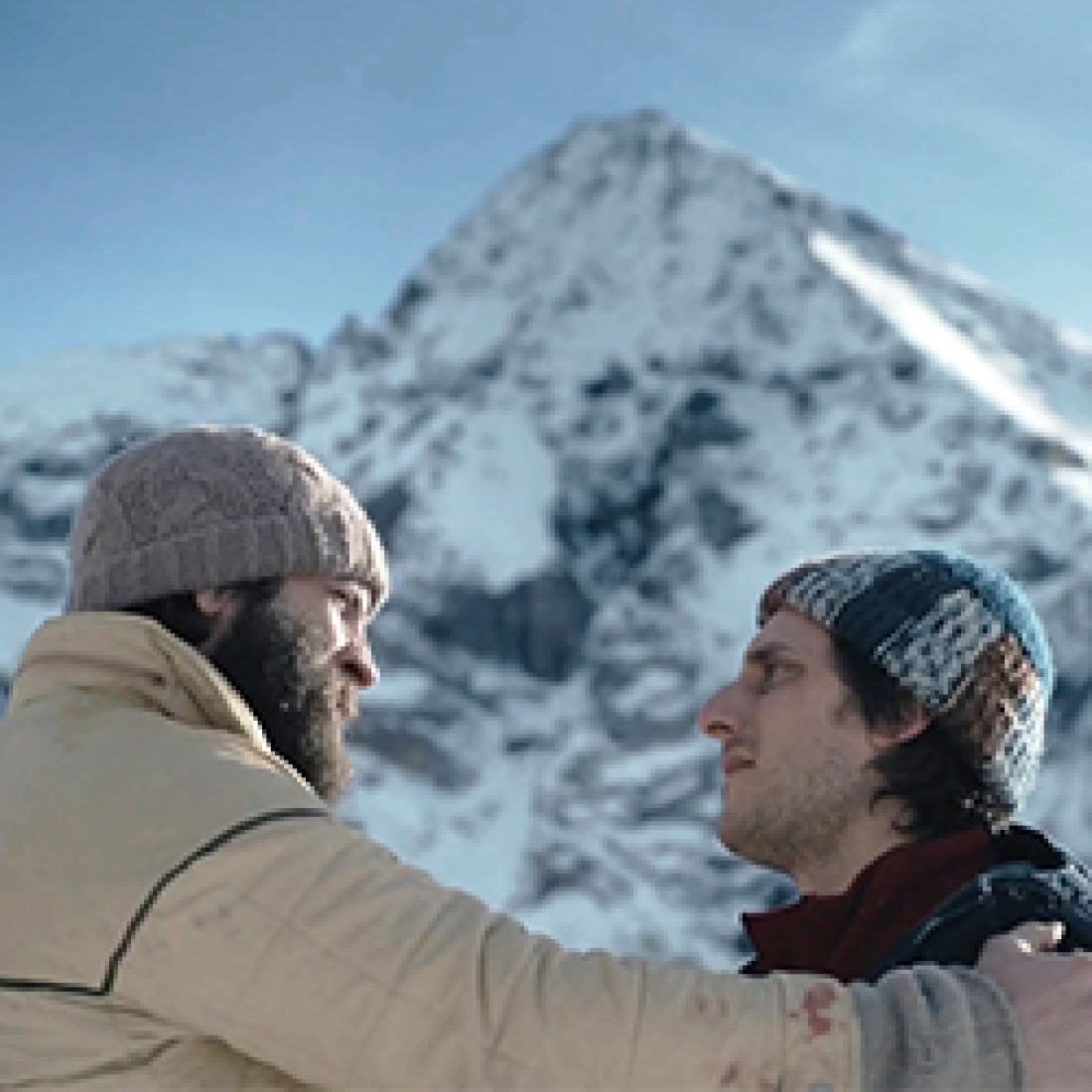 Two male friends in beanies stand at base of snowy Alps