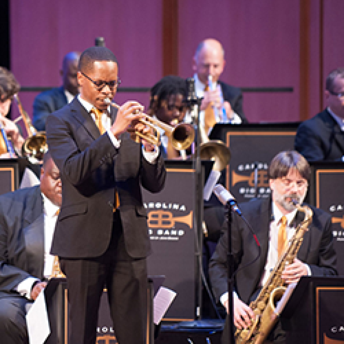 Man playing trumpet while standing next to other seated musicians