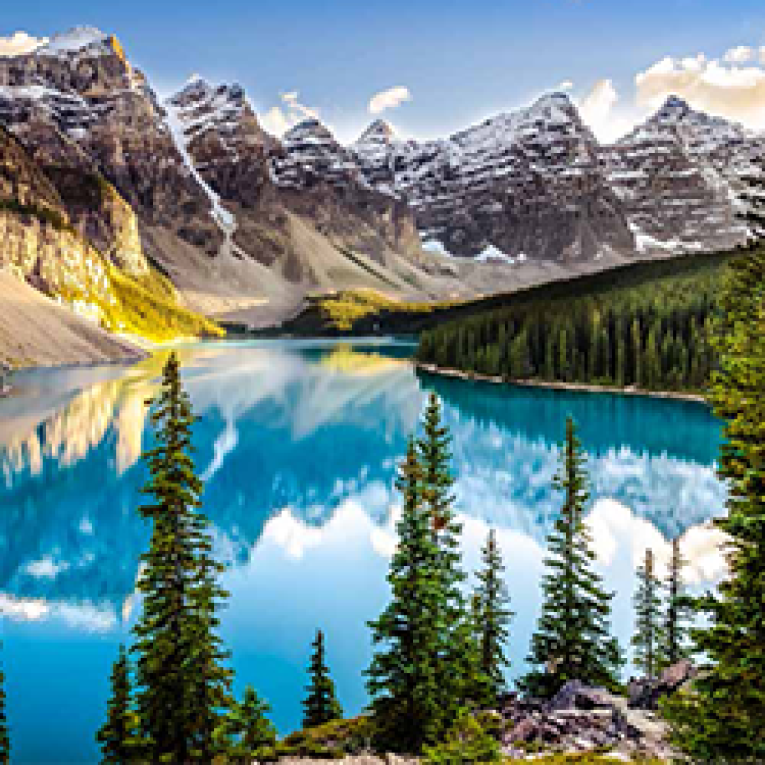 Picturesque view of Canadian Rockies topped with snow behind a pristine lake and trees