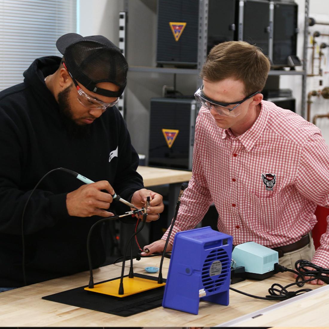 Male student works on engineering project while observed by male instructor