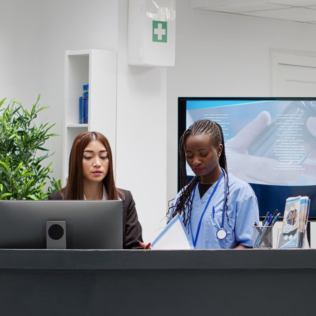 Diverse medical team working at hospital reception desk, giving assistance to patients in waiting room area on seats. Nurse and receptionist helping people in lobby, private healthcare center.
