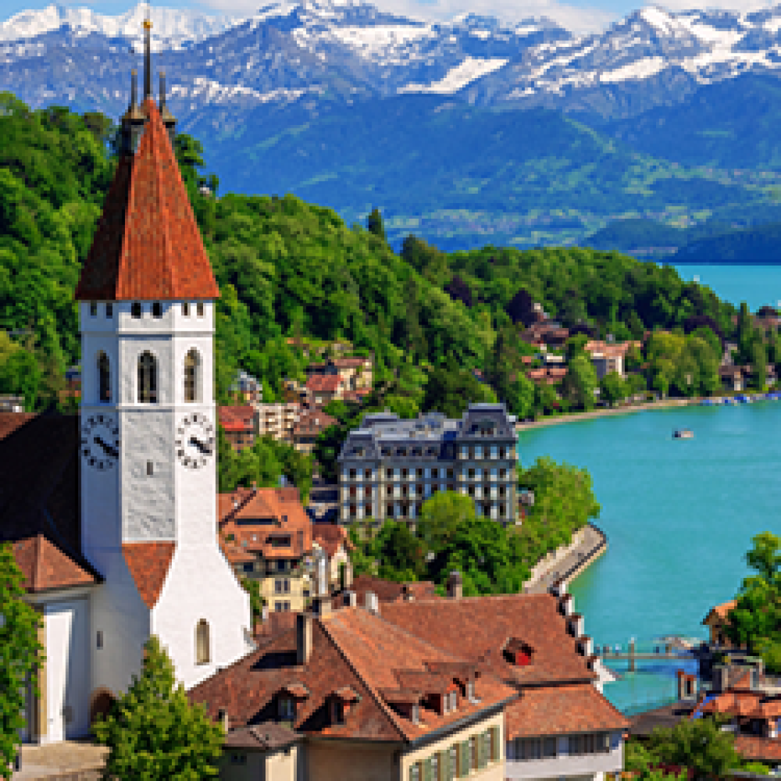 Scenic outdoor view of Swiss cathedral, blue water, buildings, trees, and mountains