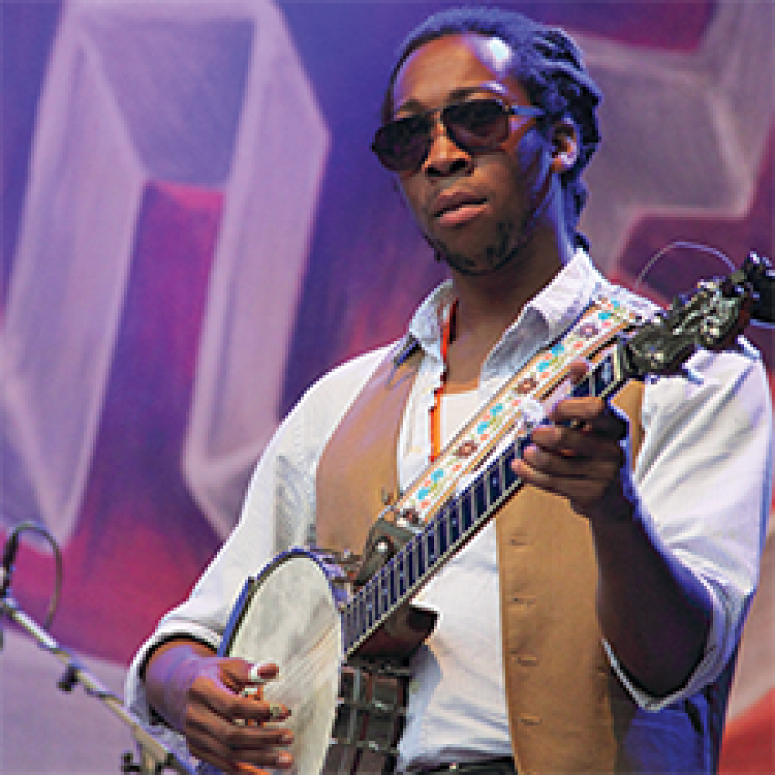 African American male in white button-up shirt, tan vest, and sunglasses, playing a banjo