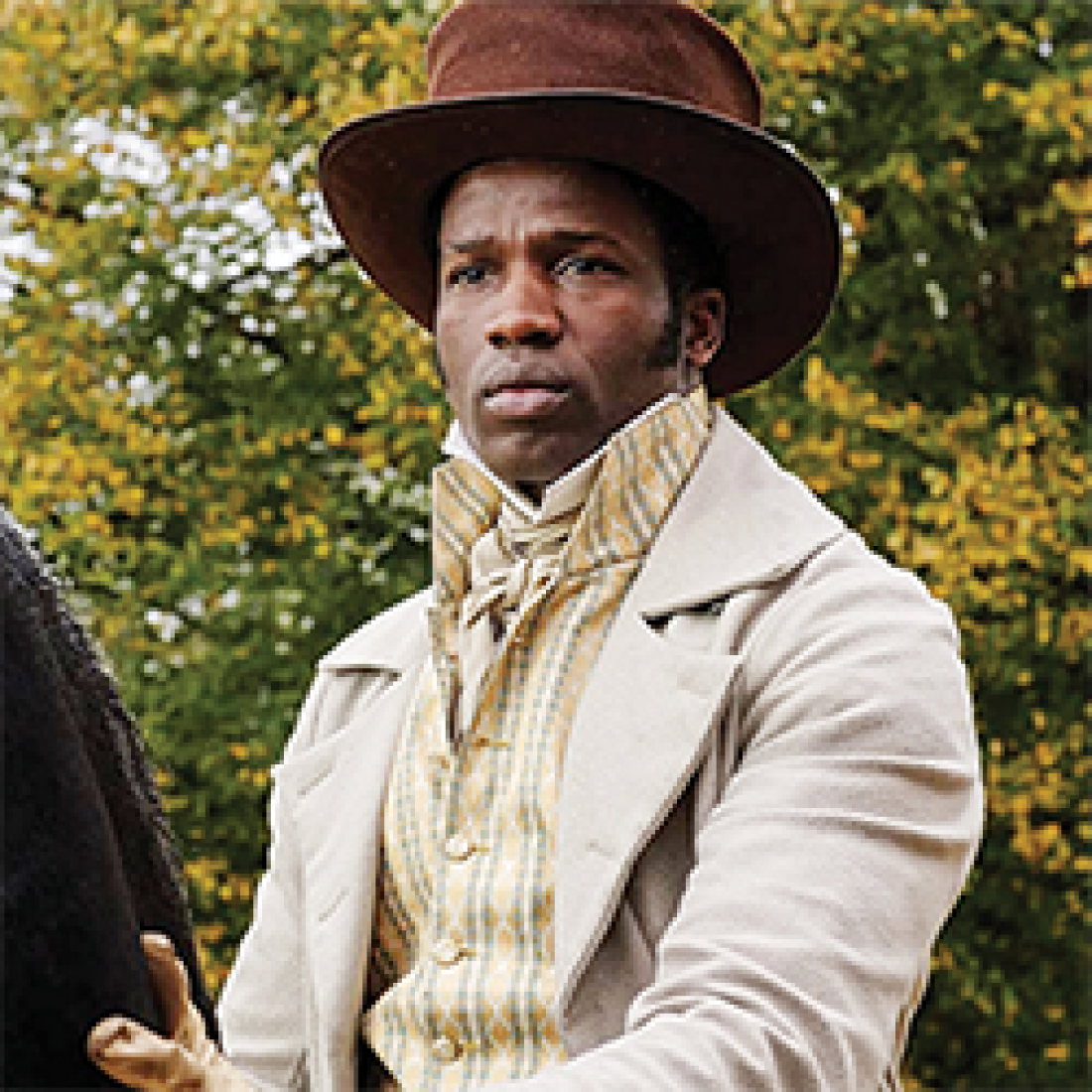 African American male in 19th century rides a horse while wearing a brown suede top hat, beige overcoat, and light yellow checkered shirt 