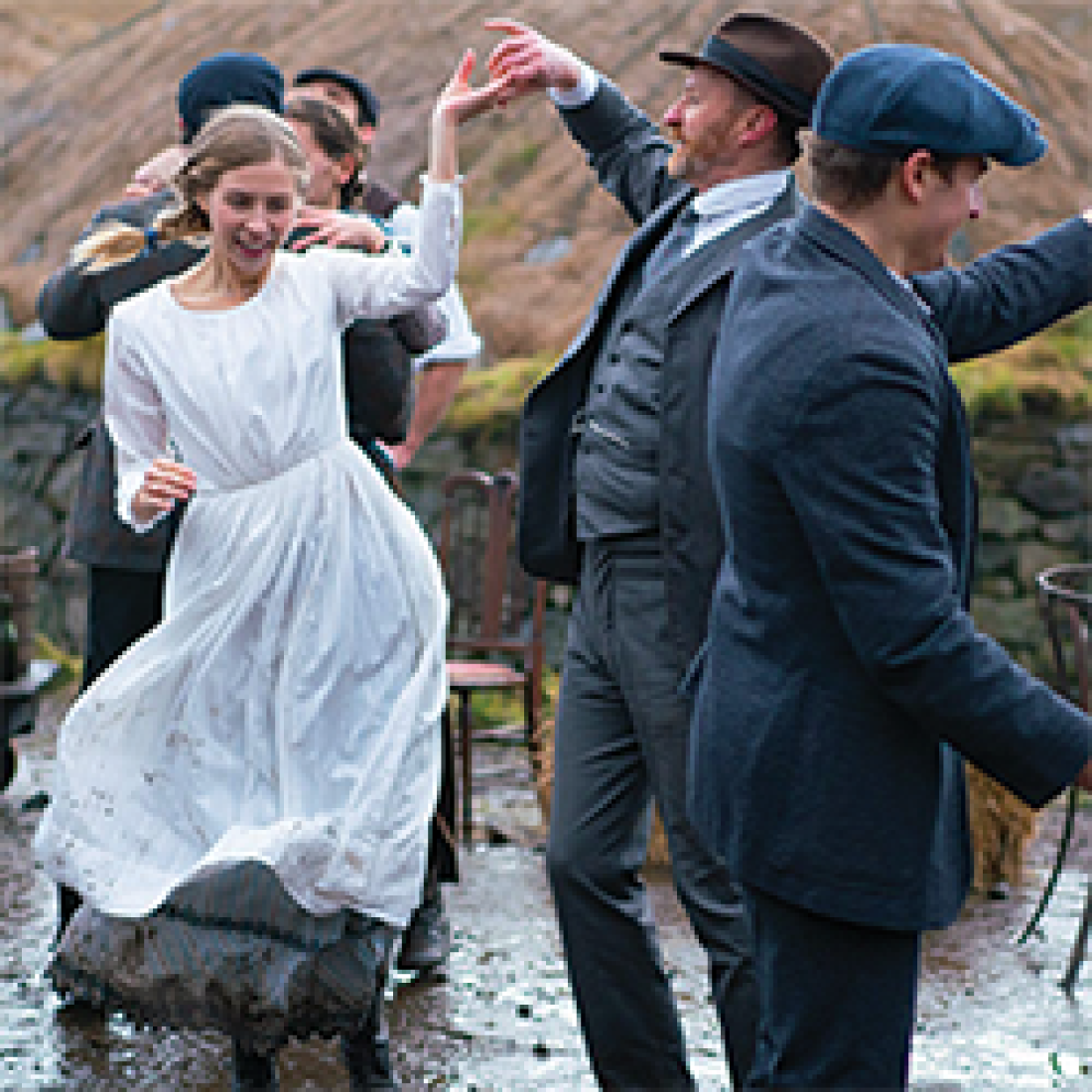 Woman in white dress dances in a shallow river with males