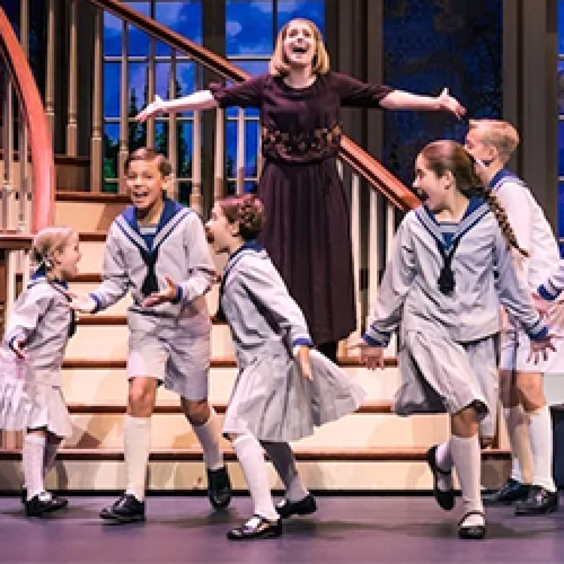 Five children and woman actress depict the Von Trapp family in The Sound of Music musical on stage by a winding staircase