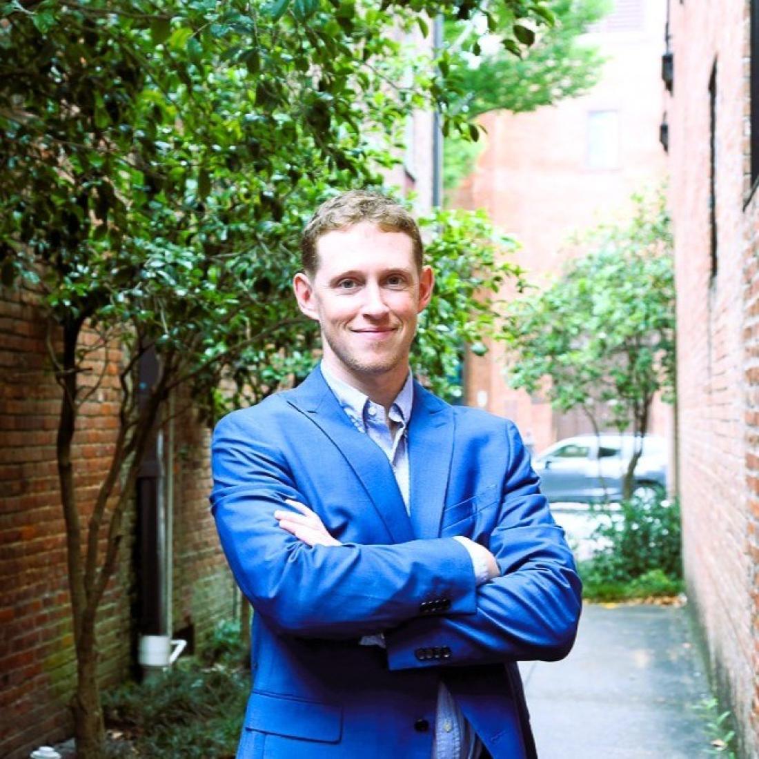 Craven alum Trevor Dunnell poses with arms crossed outside in downtown New Bern