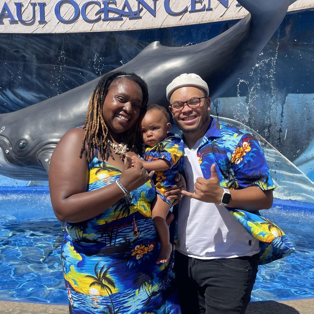 Craven CC alum Akiim Allen poses with his wife and small child wearing matching Hawaiian-patterned clothing in front of a Maui aquarium center