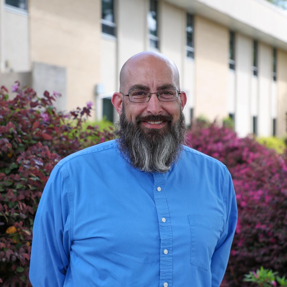 Man with beard stands smiling outside