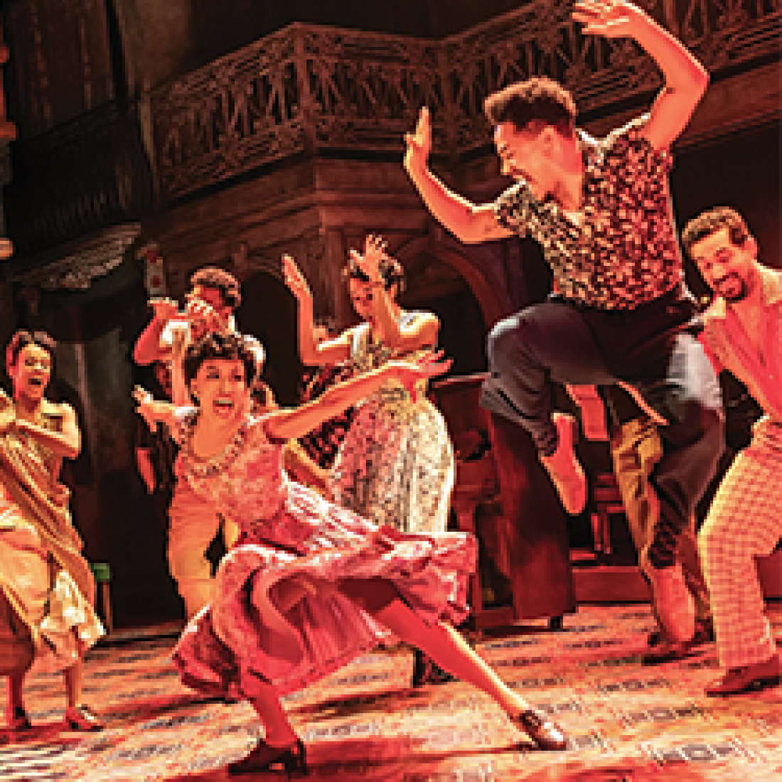 Performers dance energetically onstage during Buena Vista Social Club, with a woman in a flowing pink dress dancing at center as the ensemble surrounds her.