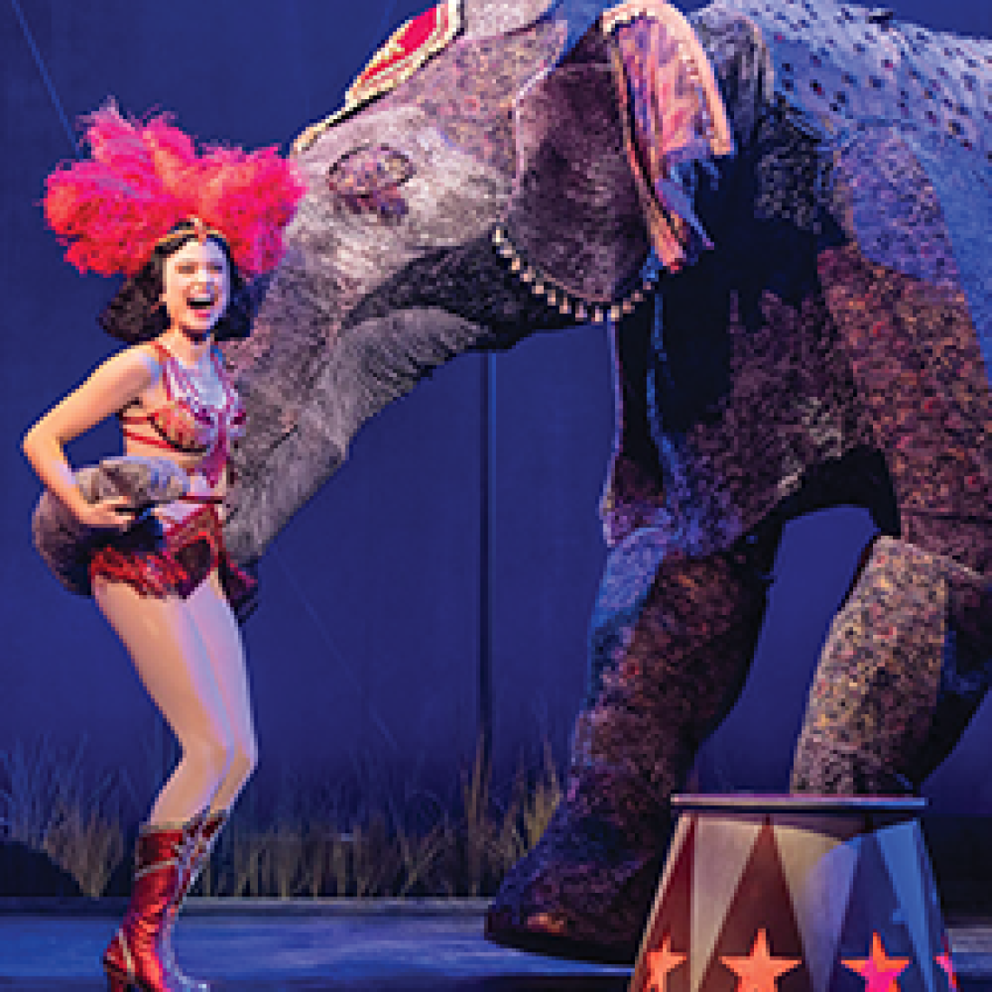 Circus performer smiles beside a life-size elephant puppet during a scene from Water for Elephants.