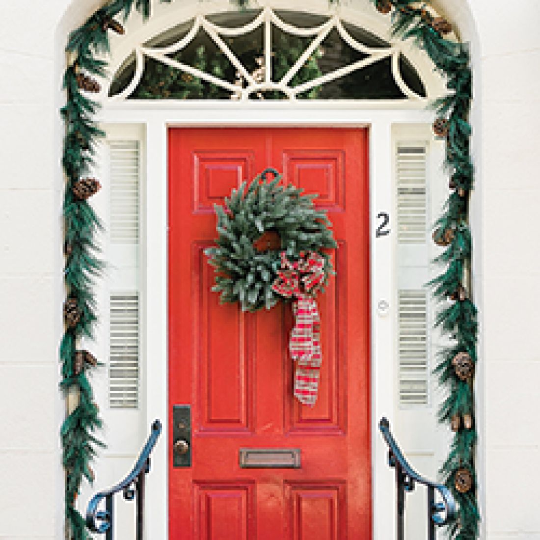 Red front door decorated with a festive evergreen wreath and garland around the white entryway.