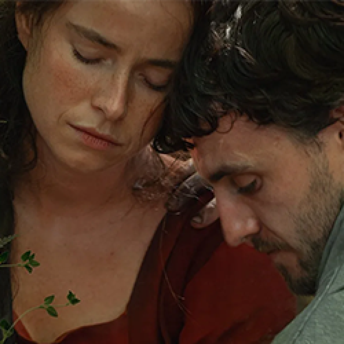 Close-up of a grieving couple leaning against one another in a tender scene from Hamnet.