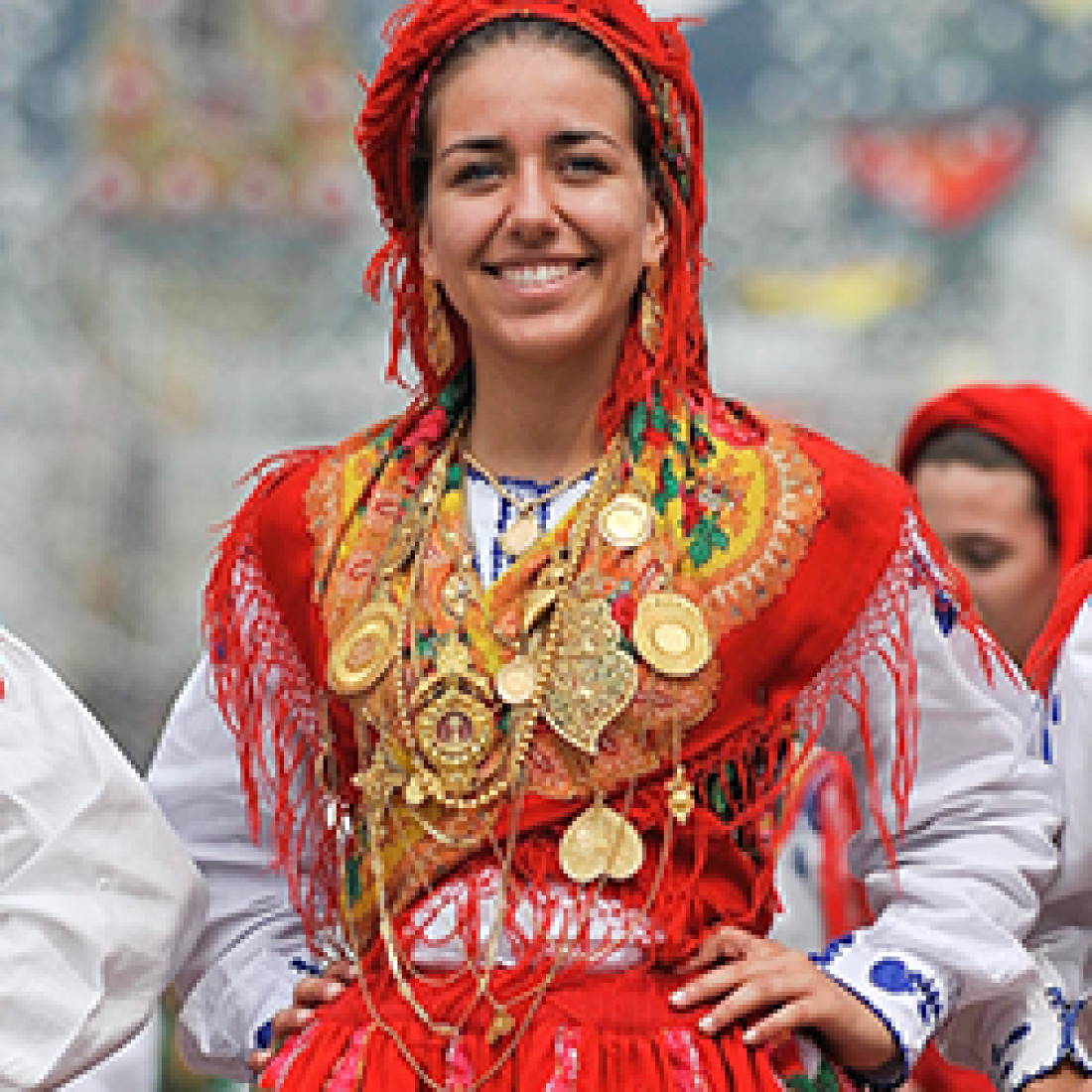Smiling woman wearing colorful traditional Portuguese clothing and jewelry during a cultural celebration.