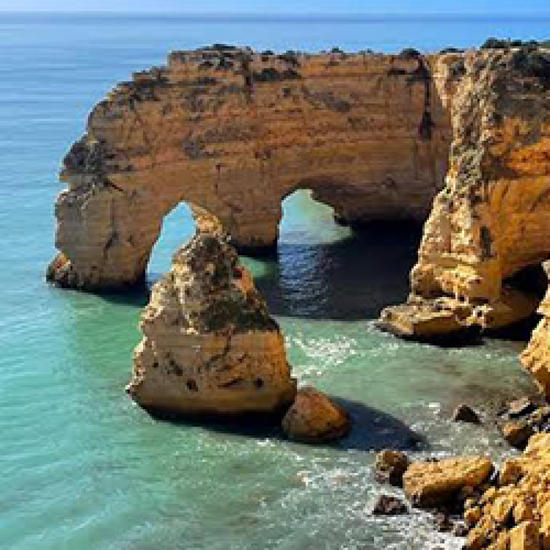 Golden limestone cliffs and natural sea arches rise above turquoise coastal waters.