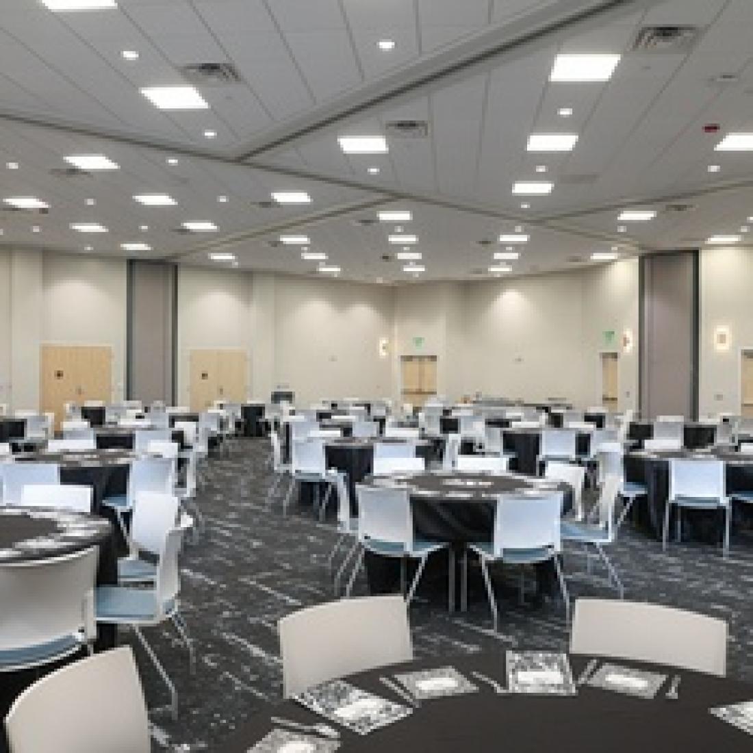 Large event space arranged with round tables and white chairs, with movable partitions dividing sections of the room.