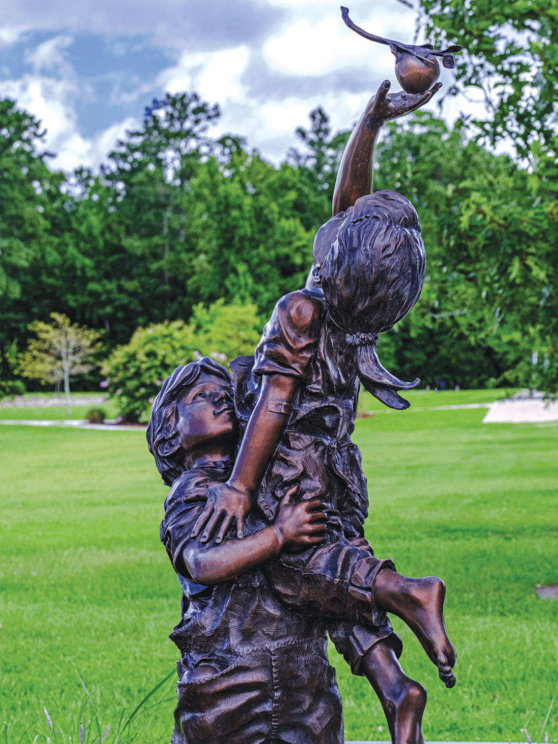 Bronze statue of boy lifting up girl to get an apple