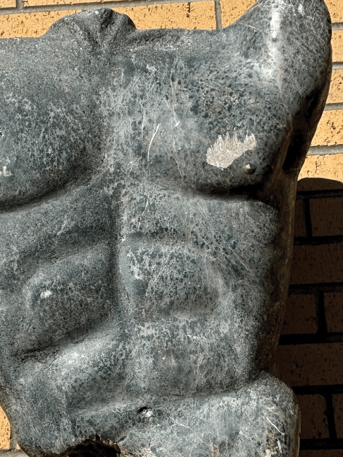 Granite sculpture of a male torso on brick exterior wall