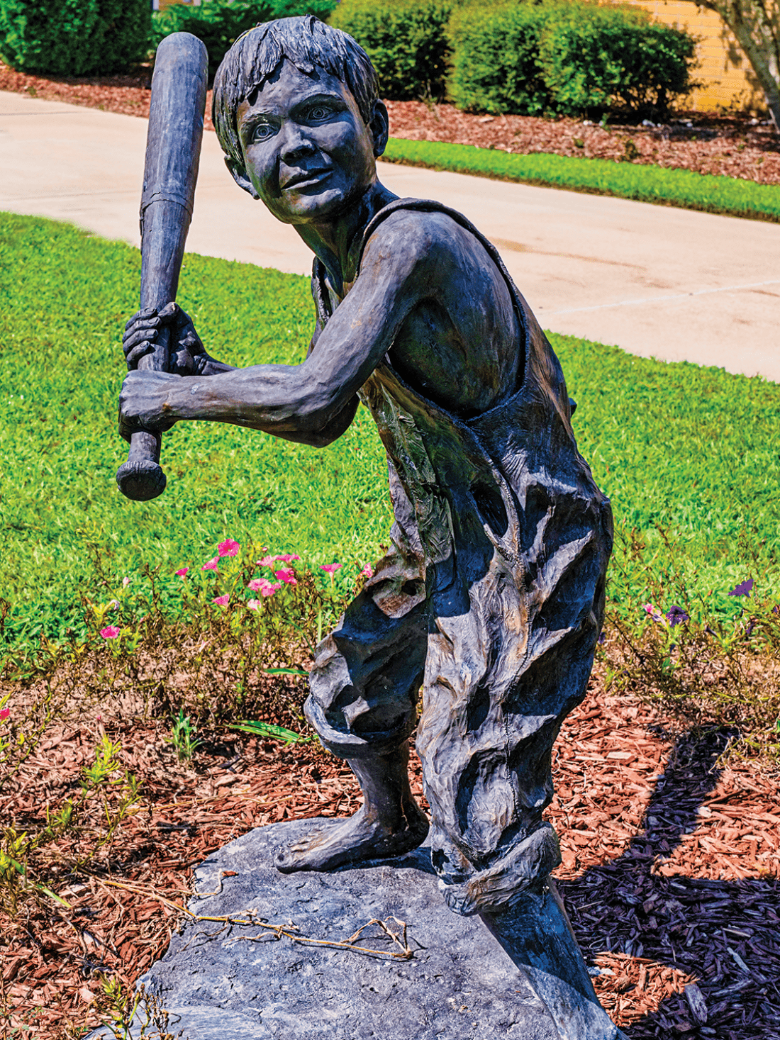 Bronze statue of little boy in overalls swinging a baseball bat