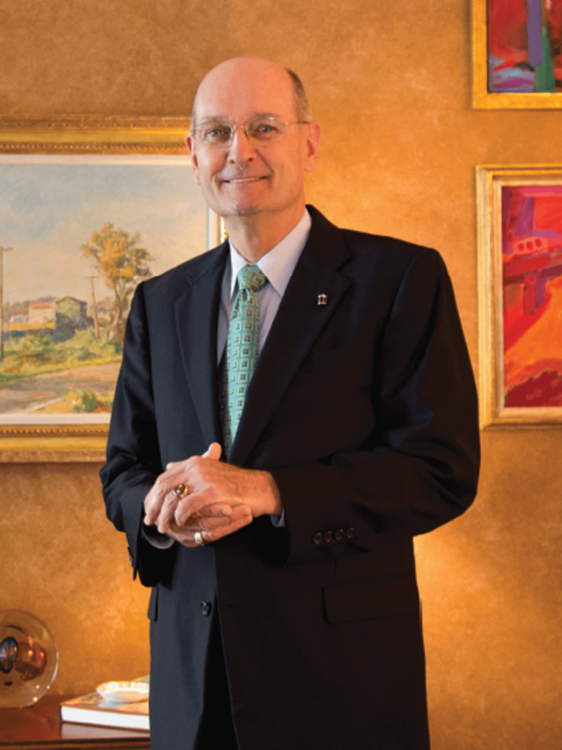 Dr. Jim Congleton wearing a suit and standing with hands clasped in a fancy foyer with paintings on the wall