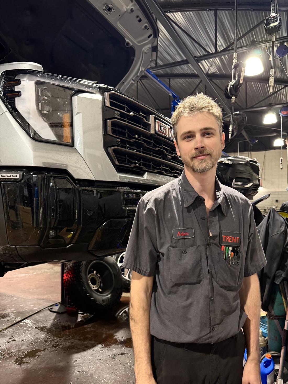 Automotive Systems Technology graduate Adam Heckman stands in front of a suspended car in the shop