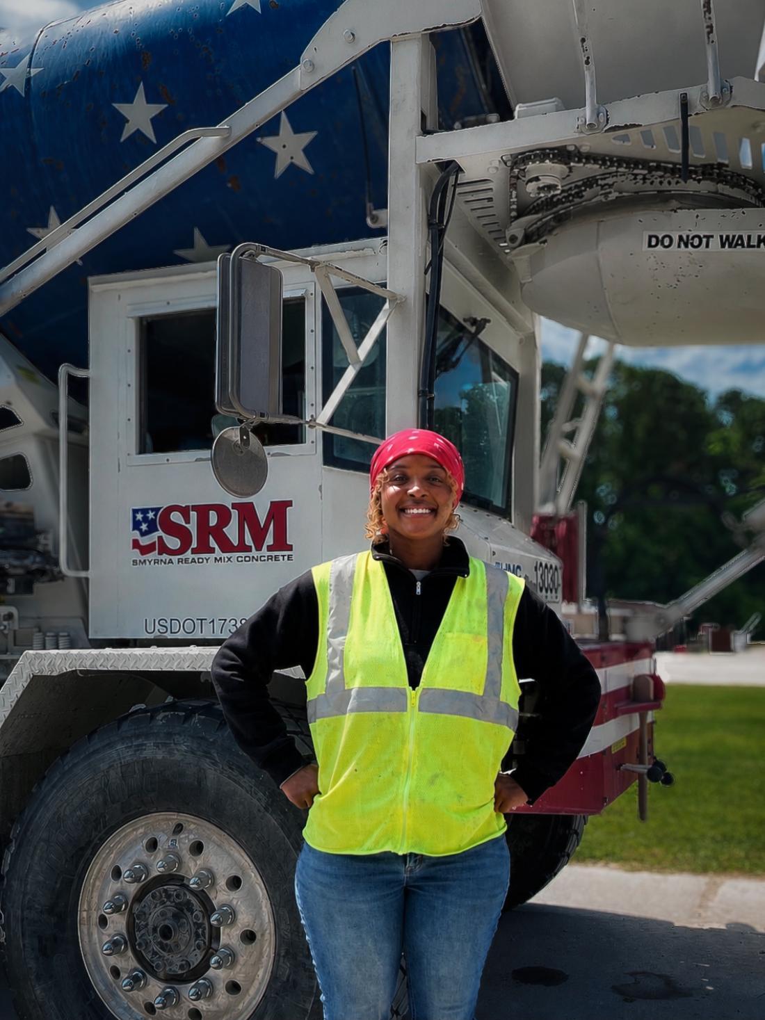 CDL program alum Dyamonesse Campell poses in a yellow safety vest while standing in front of a concrete mixer truck