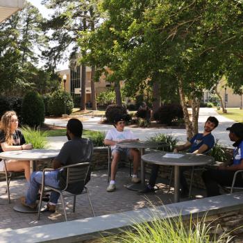 Students sitting and talking at outside tables in courtyard