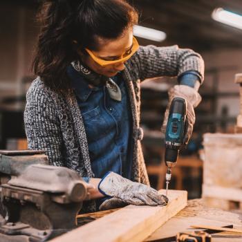 Female carpenter drills into plank of wood