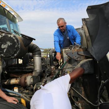 Diesel systems student works on engine outside with two instructors
