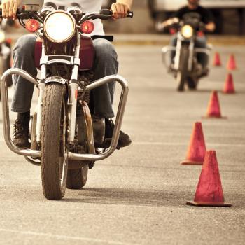 Three people riding motorcycles through cones in parking lot