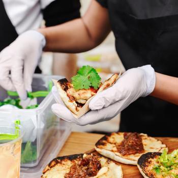 Food service worker prepares taco and tops with cilantro