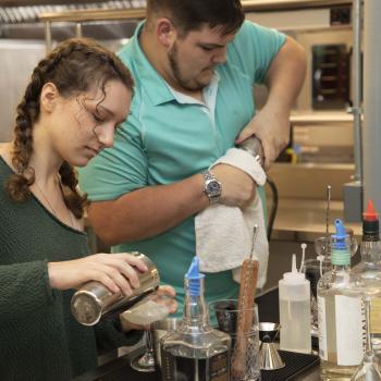 Female and male students practice mixing drinks in bartending class