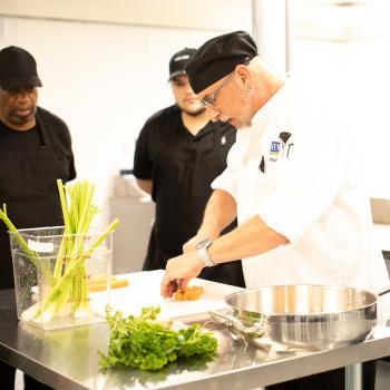 Chef instructor shows students how to chop vegetables