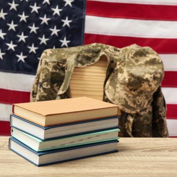 American flag behind military jacket draped on chair and stack of books