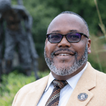 Man in suit jacket stands in front of statue
